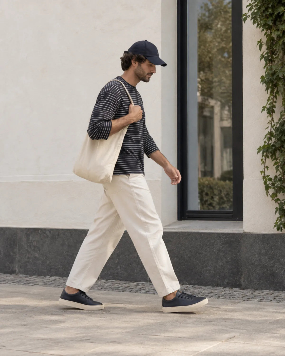 Hombre caminando con gorra, camiseta de rayas y pantalón crudo llevando las Bauhaus navy blue
