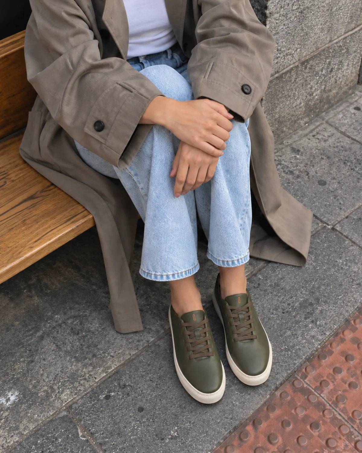 Mujer sentada en un banco con gabardina y vaqueros claros llevando las Bauhaus ever green