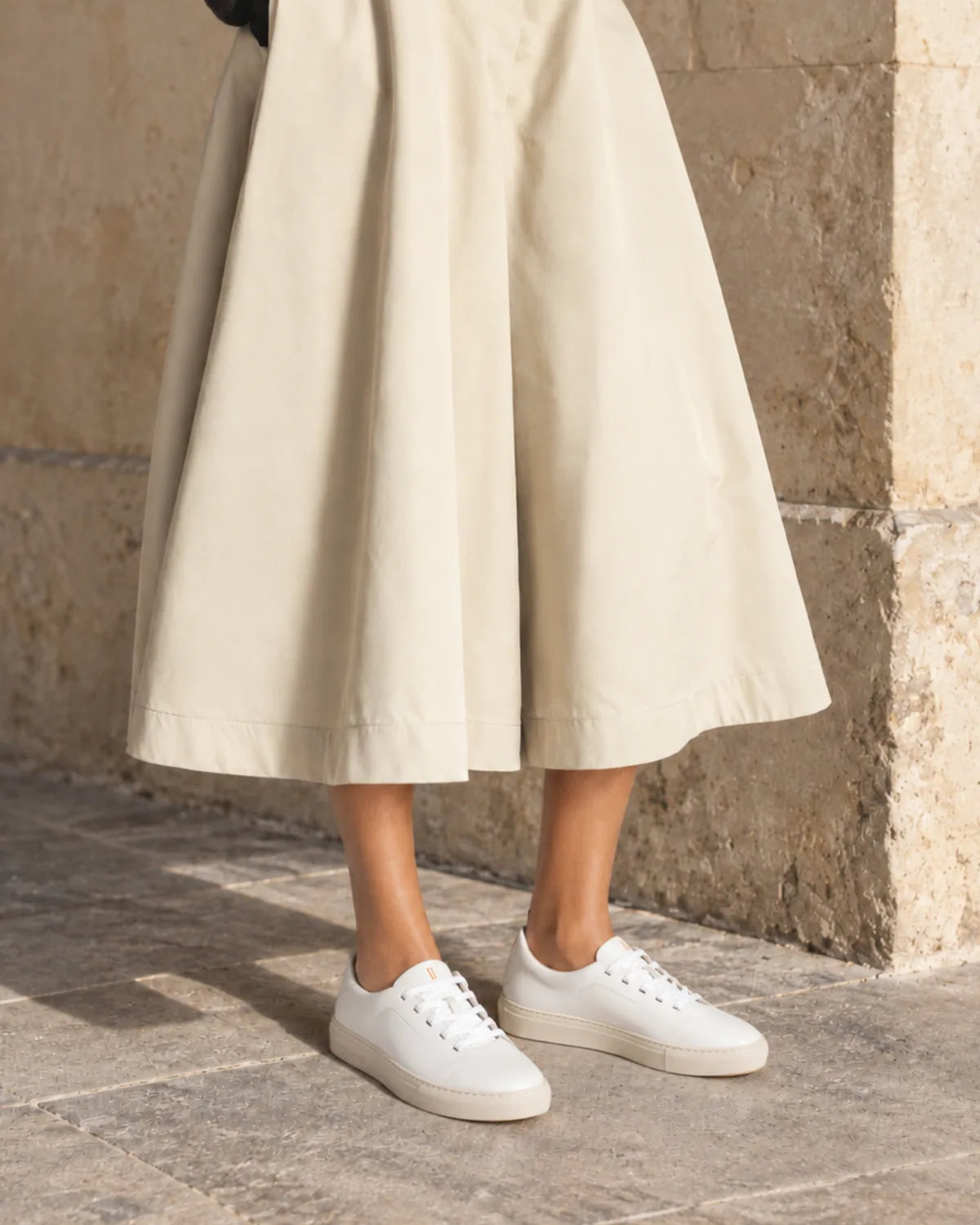 Bauhaus pure white con falda midi color crudo junto a una pared de piedra