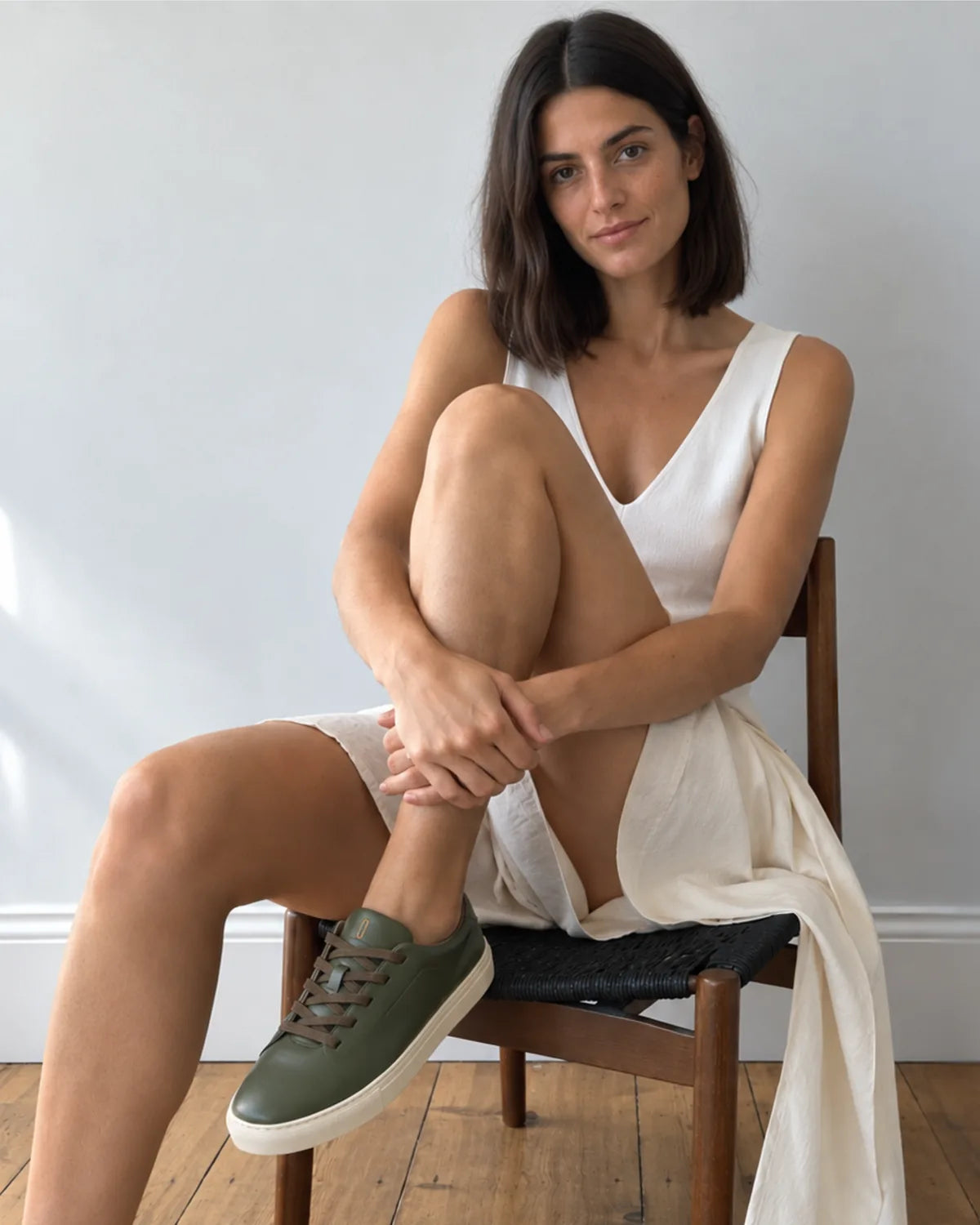 Mujer sentada en una silla de madera con vestido blanco llevando las Bauhaus ever green